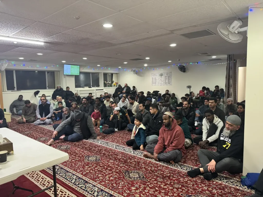 A full hall of men and boys listening to a community lecture at Aman Islamic Trust, Wellington